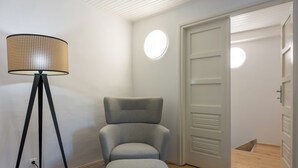 Ein Zimmer mit grauem Polsterstuhl, einer Stehlampe und einer Tür mit Lichtschalter.