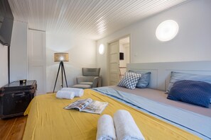 A hotel room with a bed, a chair, a table with a lamp, and a suitcase. - Veli Lošinj Old Town Apartments (Mali Losinj)