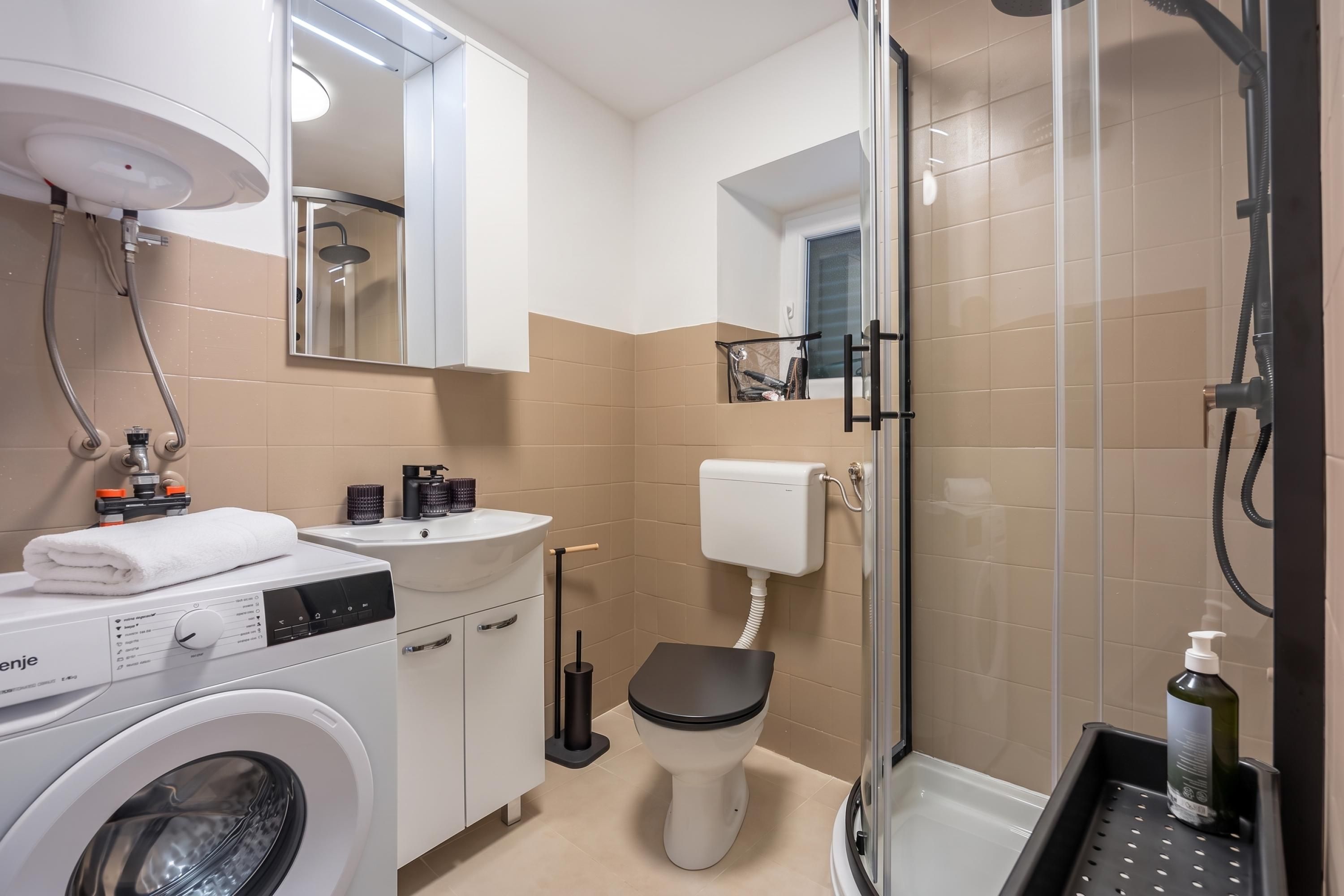 A modern bathroom with a washing machine, a sink, a toilet, and a shower area.