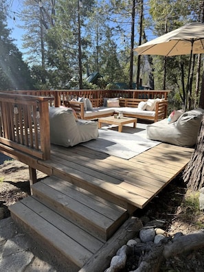 An outdoor deck with wooden furniture, including sofas and a table, surrounded by trees.