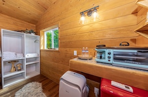 A compact kitchen with wooden walls, a window, a coffee maker, a toaster, and a small refrigerator.