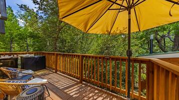A wooden deck with outdoor furniture, a large yellow umbrella, and a view of a forested area.