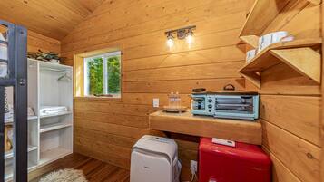 A compact kitchen with wooden walls, a window, a sink, a toaster, and a refrigerator.