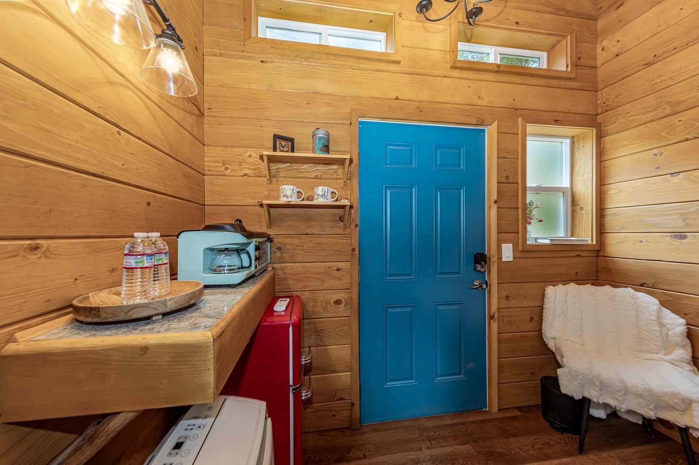 Een klein houten huisje met een kitchenette, een blauwe deur en een klein raam.