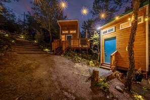 Una cabaña con un muelle de madera y una puerta azul, rodeada de árboles y un sendero de tierra.