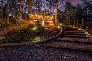 Eine Holzterrasse mit Lichterketten, umgeben von Bäumen und einem Kiesweg, der darauf führt.