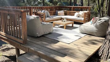 Eine Terrasse im Freien mit Holzmöbeln, darunter Sofas und ein Tisch, umgeben von Bäumen.