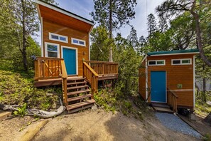 A wooden cabin with a staircase leading to a deck, surrounded by trees.