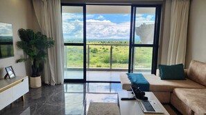 A modern living room with a large window, a sofa, a coffee table, a laptop, and a potted plant. - Sky homes 3bedroom with a park view (Syokimau)