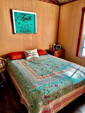 Ein Schlafzimmer mit einem Bett, einem Nachttisch, einem Radio, einem gerahmten inspirierenden Zitat und einem Fenster.
