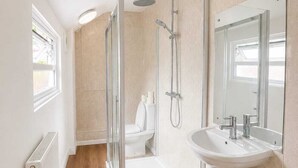Un baño moderno con ducha envuelta en vidrio, un lavamanos pedestal blanco y un espejo grande.