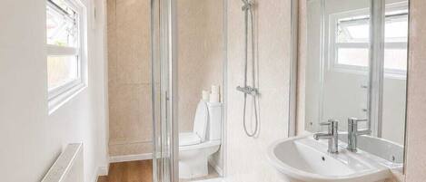 A modern bathroom with a glass-enclosed shower, a white pedestal sink, and a large mirror.