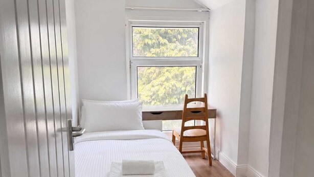 Un dormitorio con cama, ventana, silla y lámpara colgante.