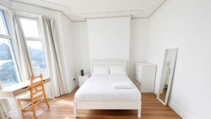 Un dormitorio con cama, escritorio, silla, cómoda y un espejo grande.