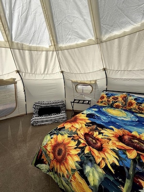 A tent with a bed featuring a sunflower print, a black and white patterned cushion, and a small table. - Enchanting Bell Tent with Stargazing and Forest Views Near Wolf Creek, Oregon (Wolf Creek)
