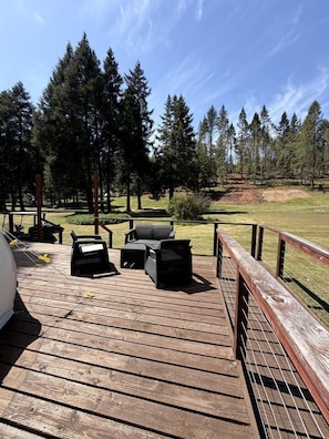 A wooden deck with outdoor furniture, a grill, and a view of a forested area.