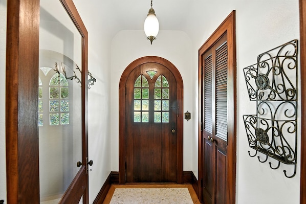 Une porte en bois avec un panneau de verre, un luminaire au-dessus et un élément décoratif en métal sur le mur.