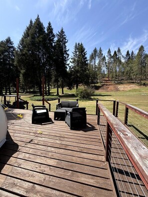 Eine Holzterrasse mit Gartenmöbeln, einem Grill und Blick auf eine bewaldete Landschaft.