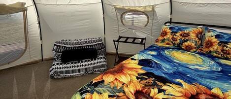 Una tienda de campaña con una cama que tiene estampado de girasol, un cojín de estampado blanco y negro y una pequeña mesa.