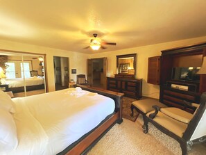 Ein Hotelzimmer mit einem Bett, einem Schreibtisch, einem Sessel, einem Fernseher und einem Deckenventilator.