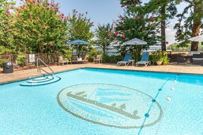 Ein Swimmingpool mit Liegestühlen und Sonnenschirmen, umgeben von Bäumen und einem Zaun.