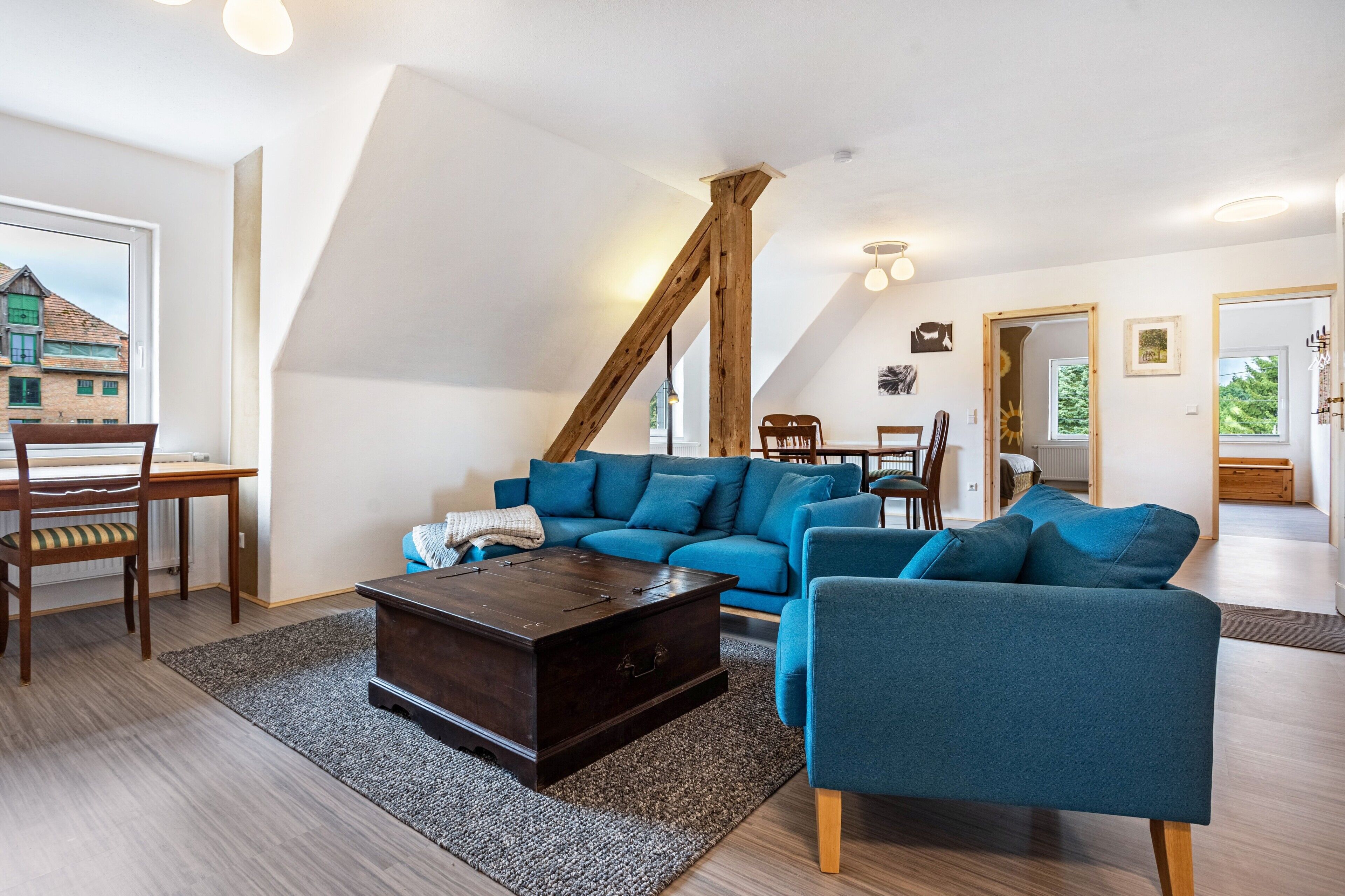 A modern living room with a blue sofa set, a wooden coffee table, and a dining area with chairs and a table.