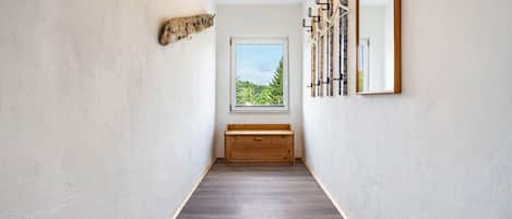 A hallway with a wooden bench, a window with a view, and wall-mounted hooks.