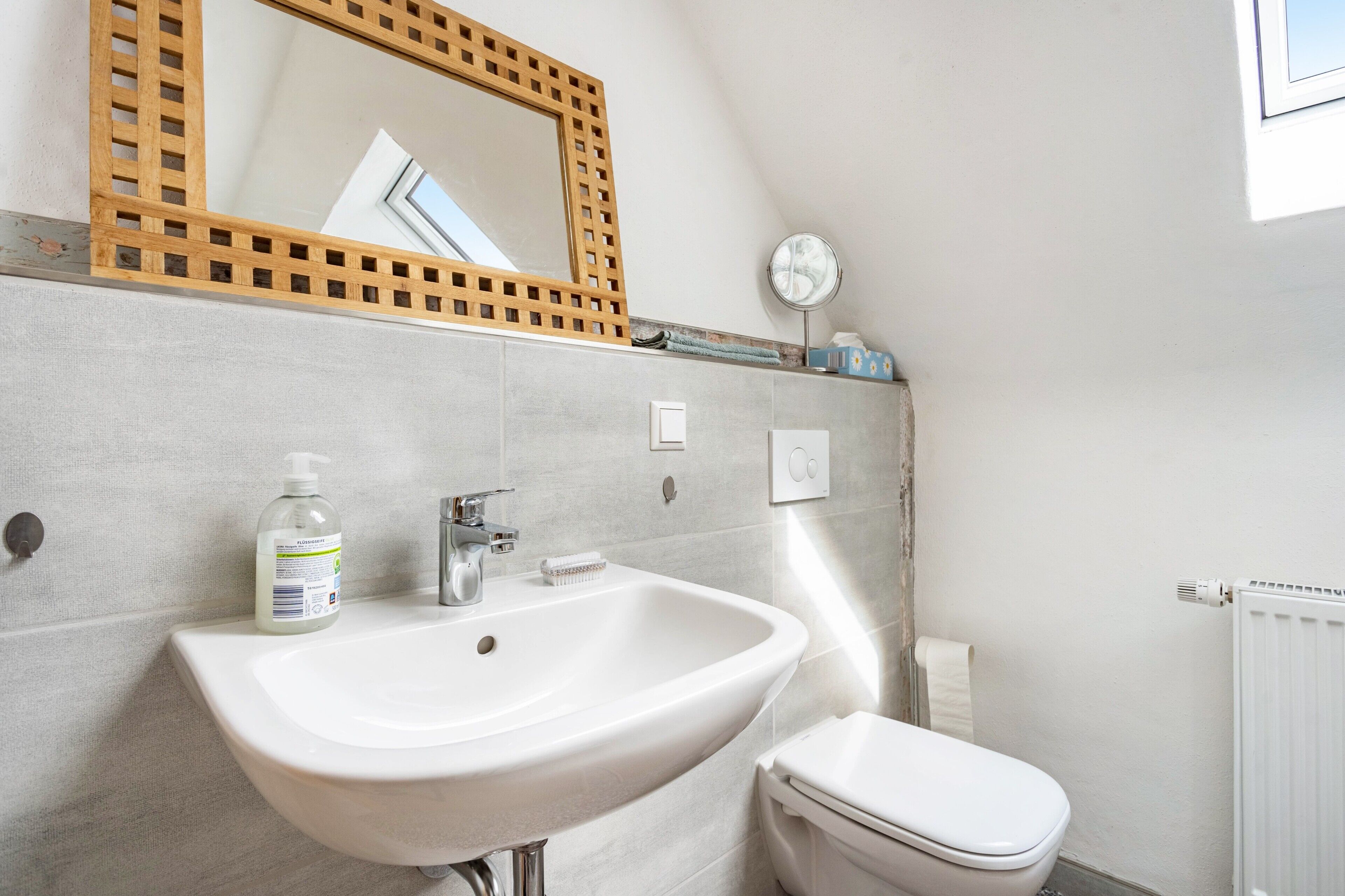 Un bagno con un lavandino bianco, un water, uno specchio e una finestra.