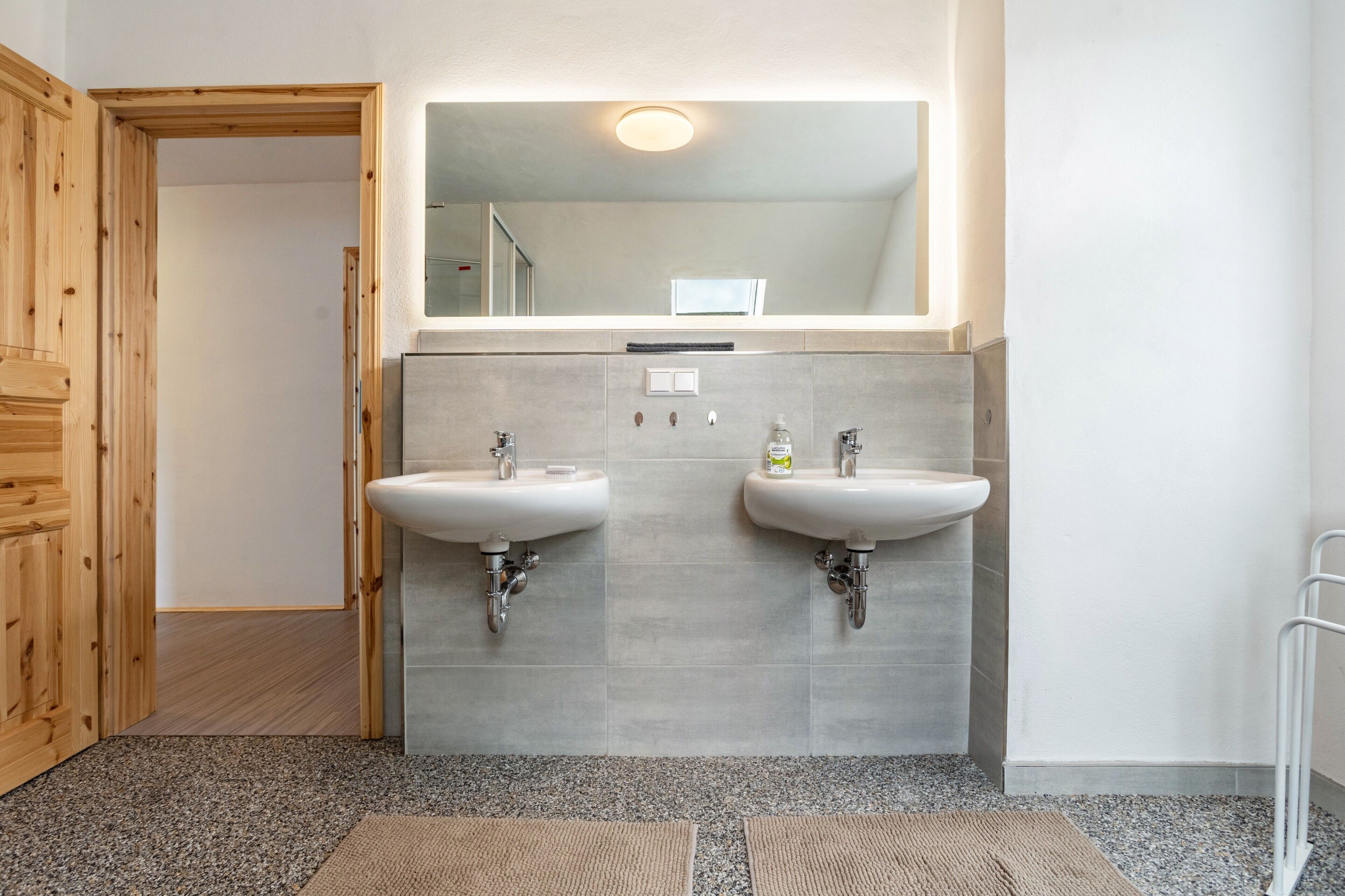 A bathroom with two sinks, a mirror above, and a door leading to another room.