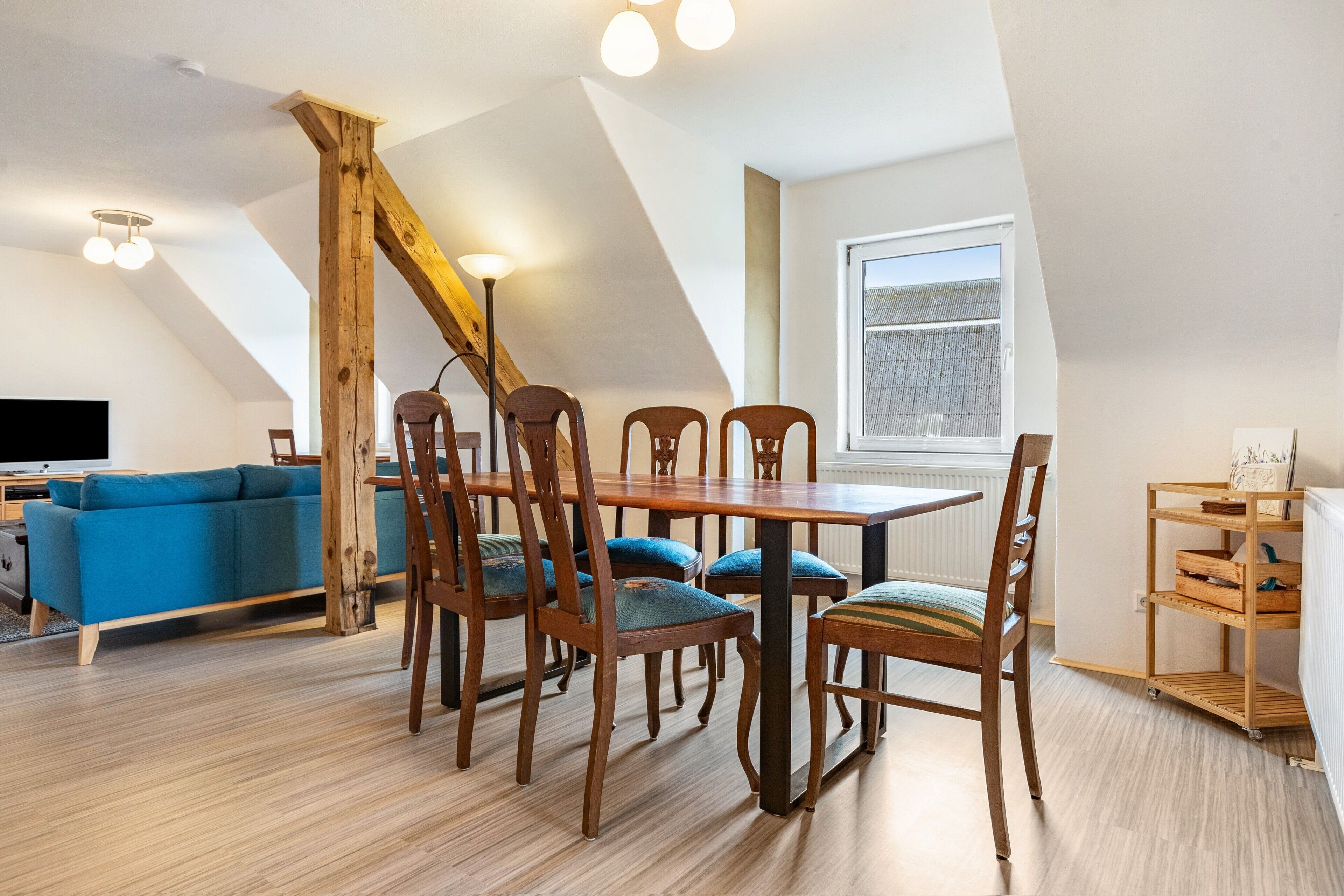 Ein Essbereich mit Holztisch und -stühlen, einem blauen Sofa und einem Fernseher in einer Ecke.