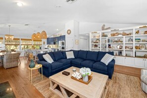 Una sala moderna con un sofá modular, una mesa de centro y una cocina al fondo.