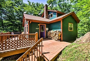 A cabin with a wooden deck, a chimney, and a stack of firewood. - Spacious Vacation Cabin with a Fire Pit in Bryson City, North Carolina (Bryson City)
