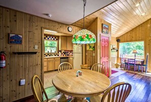 A wooden interior with a round dining table, chairs, a kitchen with a checkered backsplash, and a colorful stained glass ceiling light. - Spacious Vacation Cabin with a Fire Pit in Bryson City, North Carolina (Bryson City)