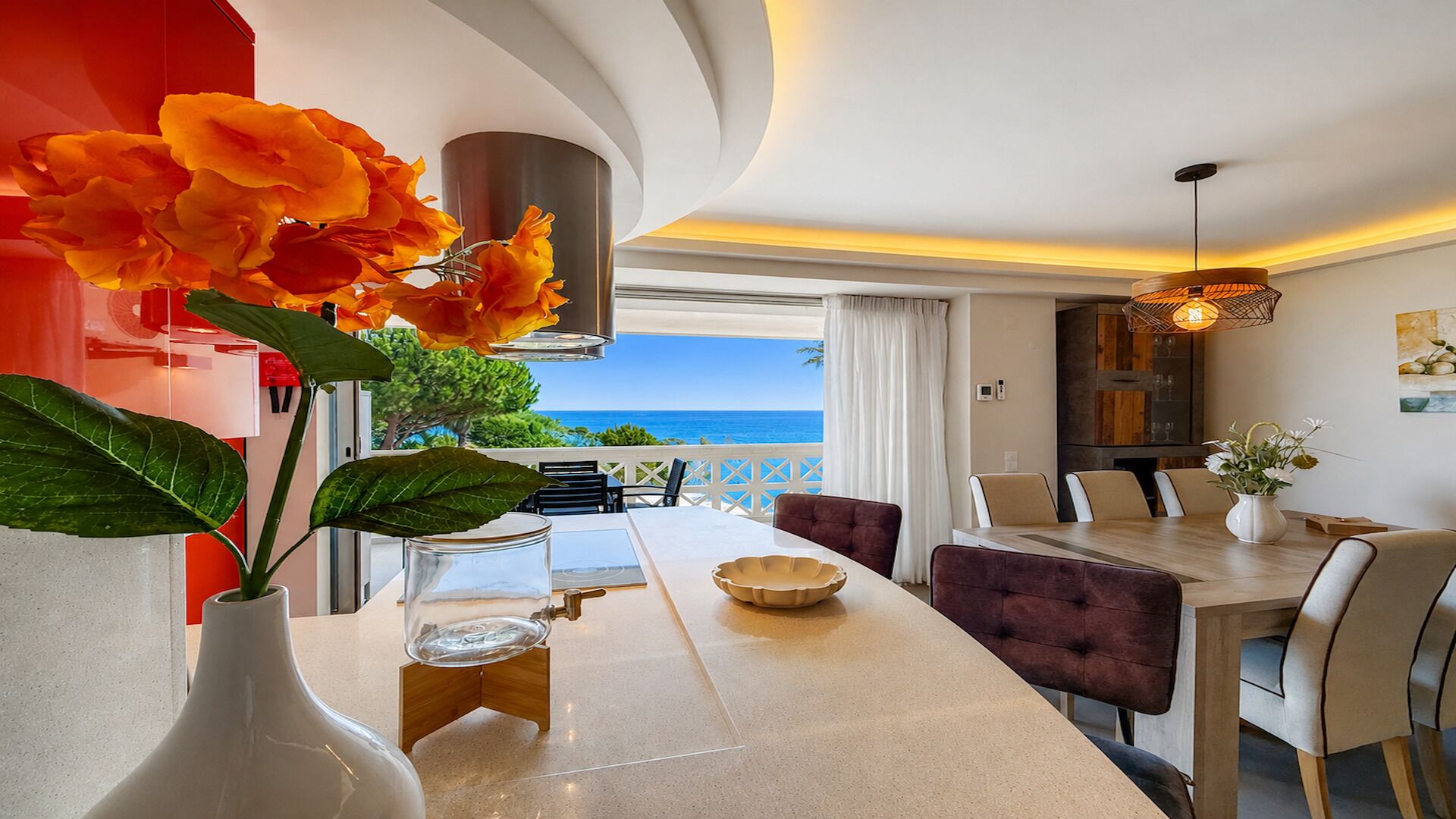 Ein moderner Essbereich mit Meerblick, eine weiße Vase mit Blumen und ein Tisch mit Stühlen.