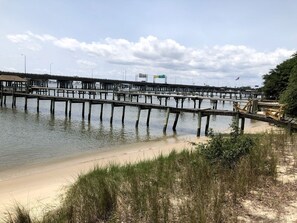 Un muelle se adentra en aguas tranquilas, con una playa de arena en primer plano.