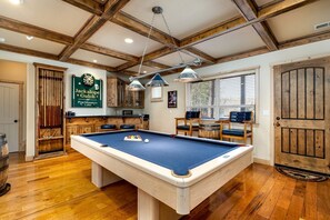 A pool table in a room with wooden floors, a bar area, and a door with a rustic design.