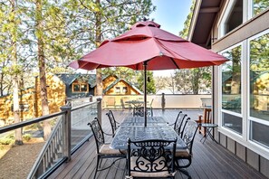 A deck with a table and chairs, a red umbrella, and a view of cabins.