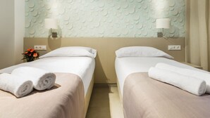 Habitación de hotel con dos camas, una pared con textura, una lámpara y un florero.