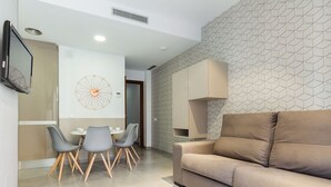 Una sala de estar moderna con un sofá color beige, un comedor con una mesa redonda y sillas, y una pared con estampado geométrico.