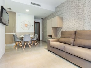Ein modernes Wohnzimmer mit einem beigefarbenen Sofa, einem Essbereich mit rundem Tisch und Stühlen sowie einer Wand mit geometrischem Muster.