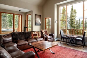 A spacious living room with a large window, a wooden coffee table, leather sofas, and a chess table.