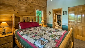 Une chambre dans une cabane en bois, avec un lit, des tables de chevet, un ventilateur de plafond et une fenêtre.