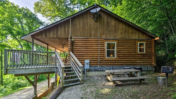 Une cabane en rondins avec un porche, un escalier, une table de pique-nique et une boîte aux lettres.