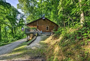 Une cabane en bois dotée d’un porche et d’un escalier menant à l’entrée, entourée d’une forêt dense.