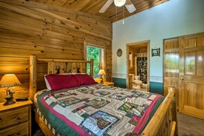 Une chambre dans une cabane en bois, avec un lit, des tables de chevet, un ventilateur de plafond et une fenêtre.