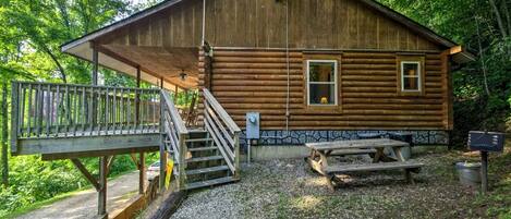 Une cabane en rondins avec un porche, un escalier, une table de pique-nique et une boîte aux lettres.