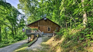 Une cabane en bois dotée d’un porche et d’un escalier menant à l’entrée, entourée d’une forêt dense.