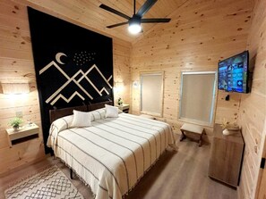 A wooden-paneled bedroom with a bed, bedside tables, a ceiling fan, and a TV mounted on the wall. - Modern Cabin in Pigeon Forge for a Romantic Glamping Rendezvous (Sevierville)