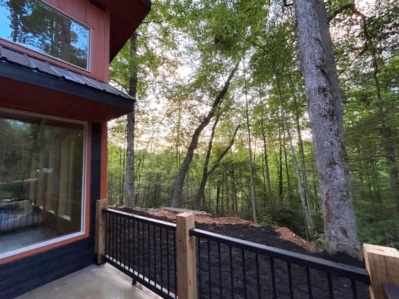 Ein modernes Gebäude mit großen Fenstern, einer Terrasse und einem Wald im Hintergrund.