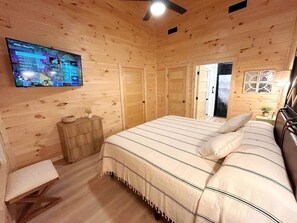 A wooden cabin bedroom with a bed, a TV, a dresser, and a bench. - Modern Cabin in Pigeon Forge for a Romantic Glamping Rendezvous (Sevierville)